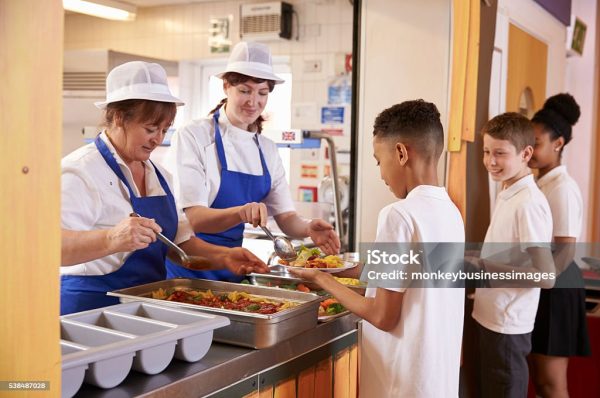 Two women serving food to a boy in a school cafeteria queue